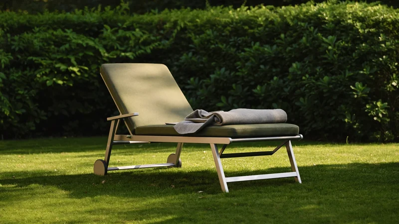 Klappbare Sonnenliege mit verstellbarer Lehne auf dem Rasen neben einer niedrigen Hecke